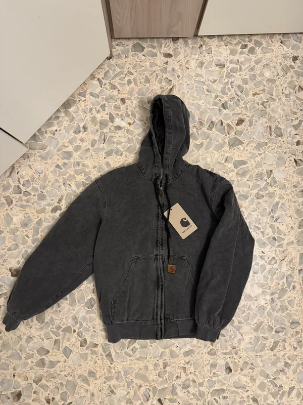 Dark hooded jacket laid flat on a stone-pattern floor.